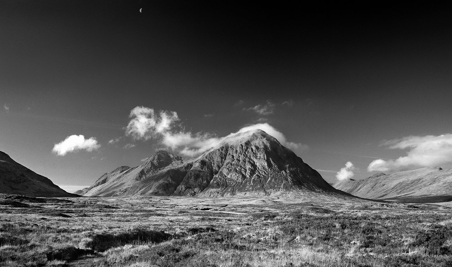 The majestic Buachaille Etive Mor captured on a winters morning showing the prestine mountain under a darkened sky under an efervesant moon lit ny the morning sun. 