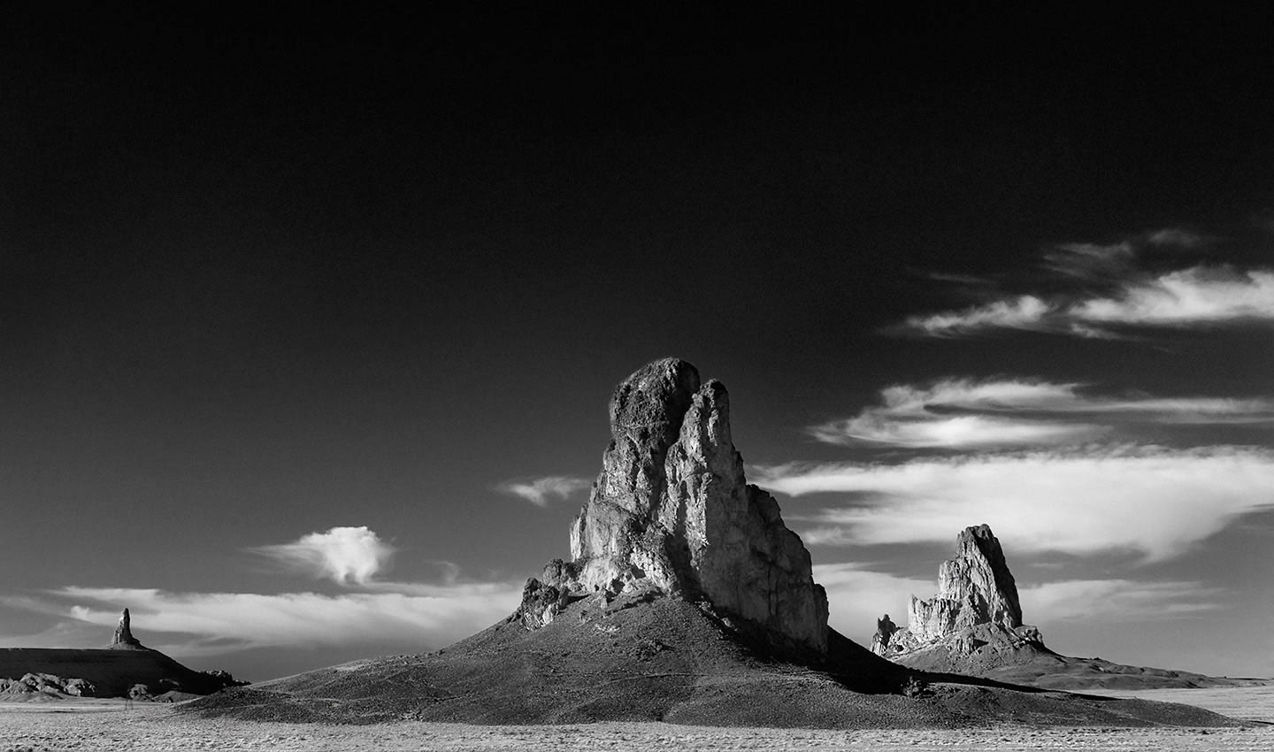 A striking photographic composition of Agathlia in Monument Valley, Utah USA, with burnt in skies against white whispy clouds.